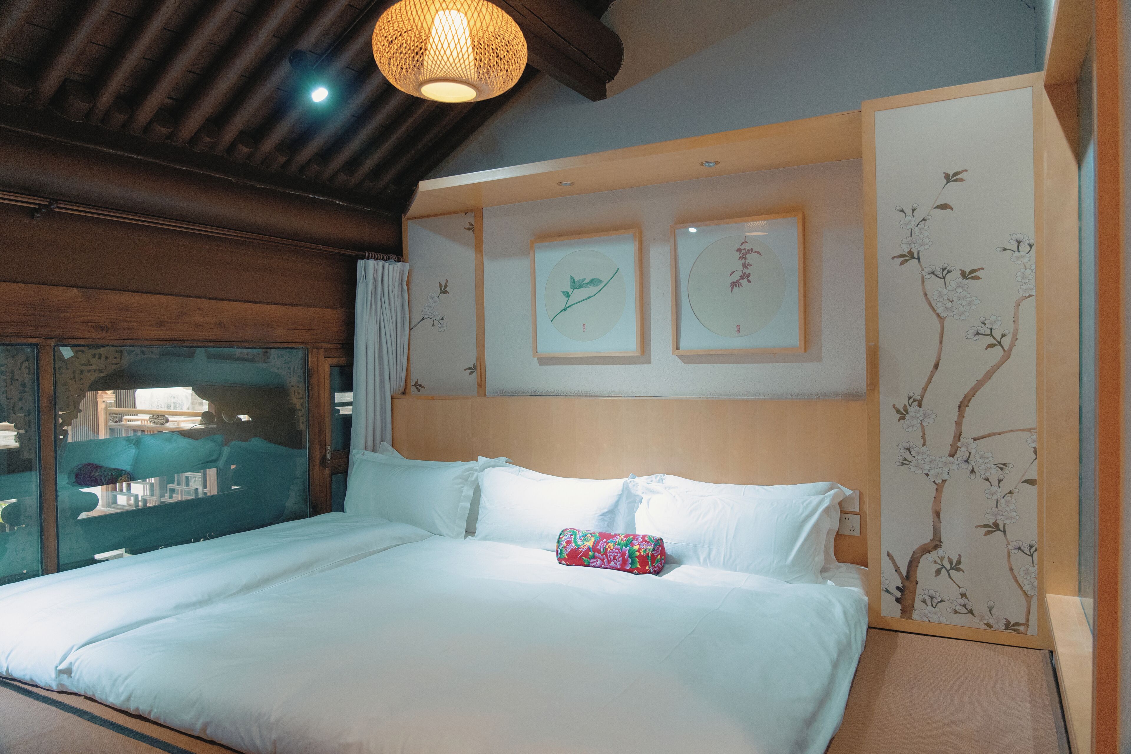 Habitación de hotel con techo de madera, cama con ropa de cama blanca e impresiones botánicas enmarcadas en la pared.