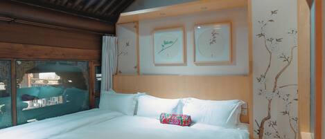 Habitación de hotel con techo de madera, cama con ropa de cama blanca e impresiones botánicas enmarcadas en la pared.