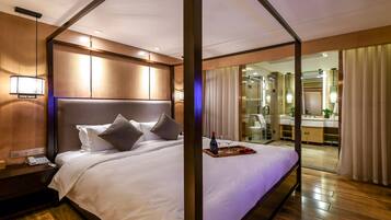 A hotel room with a large bed, a bedside table with a phone, and a tray with a bottle and glasses.