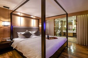 Habitación de hotel con una cama grande, una mesita de noche con teléfono y una bandeja con botella y vasos.