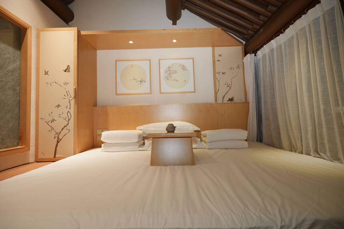 Un dormitorio con cama, almohadas, una mesita de noche y una obra de arte en la pared.