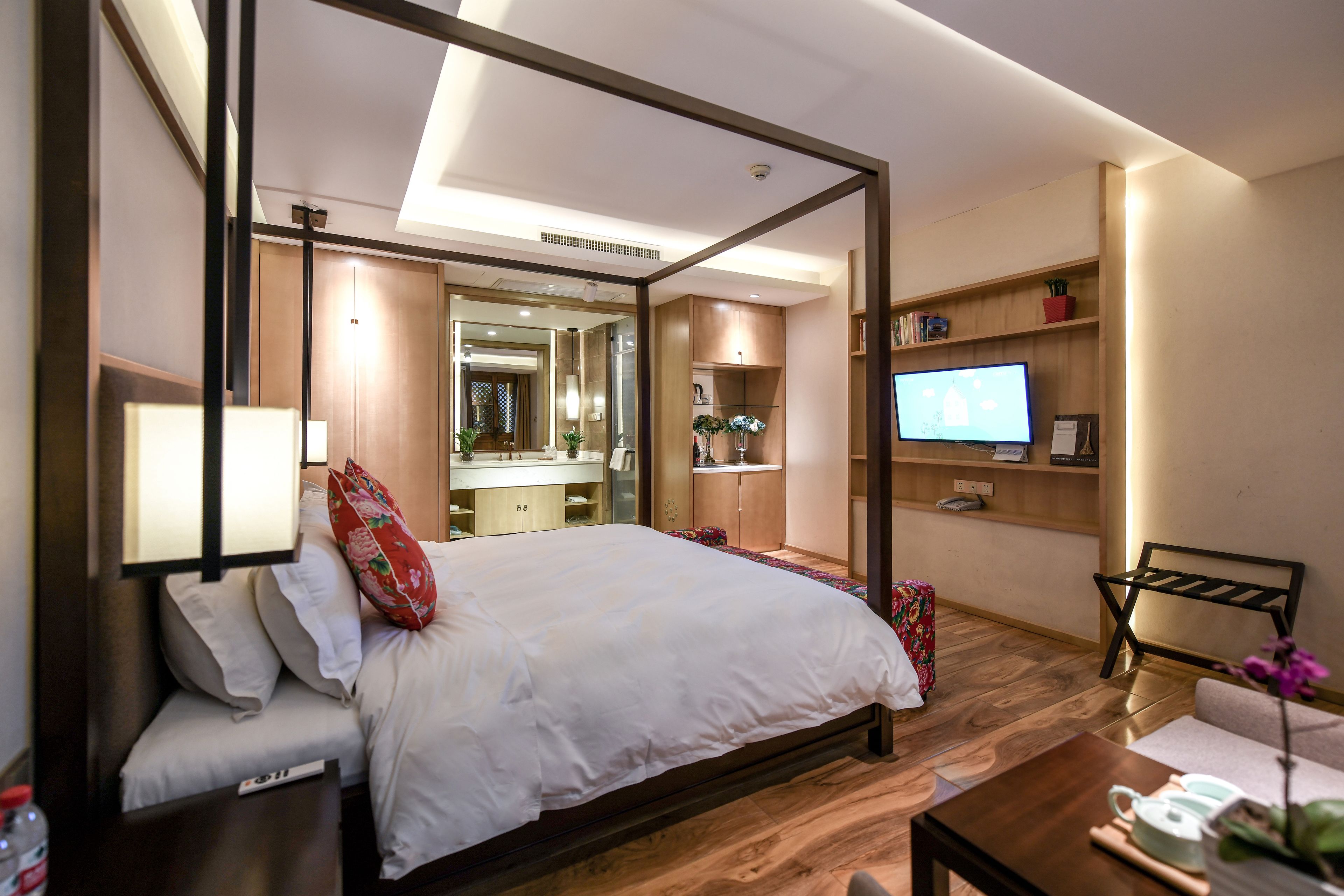 A modern hotel room with a large bed, a television, a desk, and a bathroom visible through an open door.