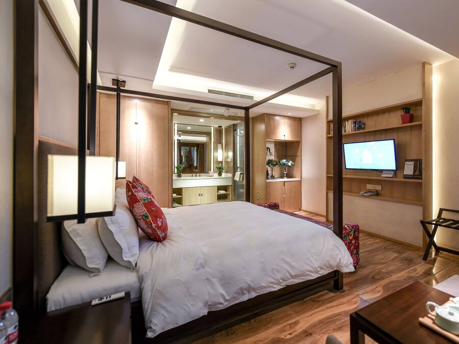 A modern hotel room with a large bed, a television, a desk, and a bathroom visible through an open door.
