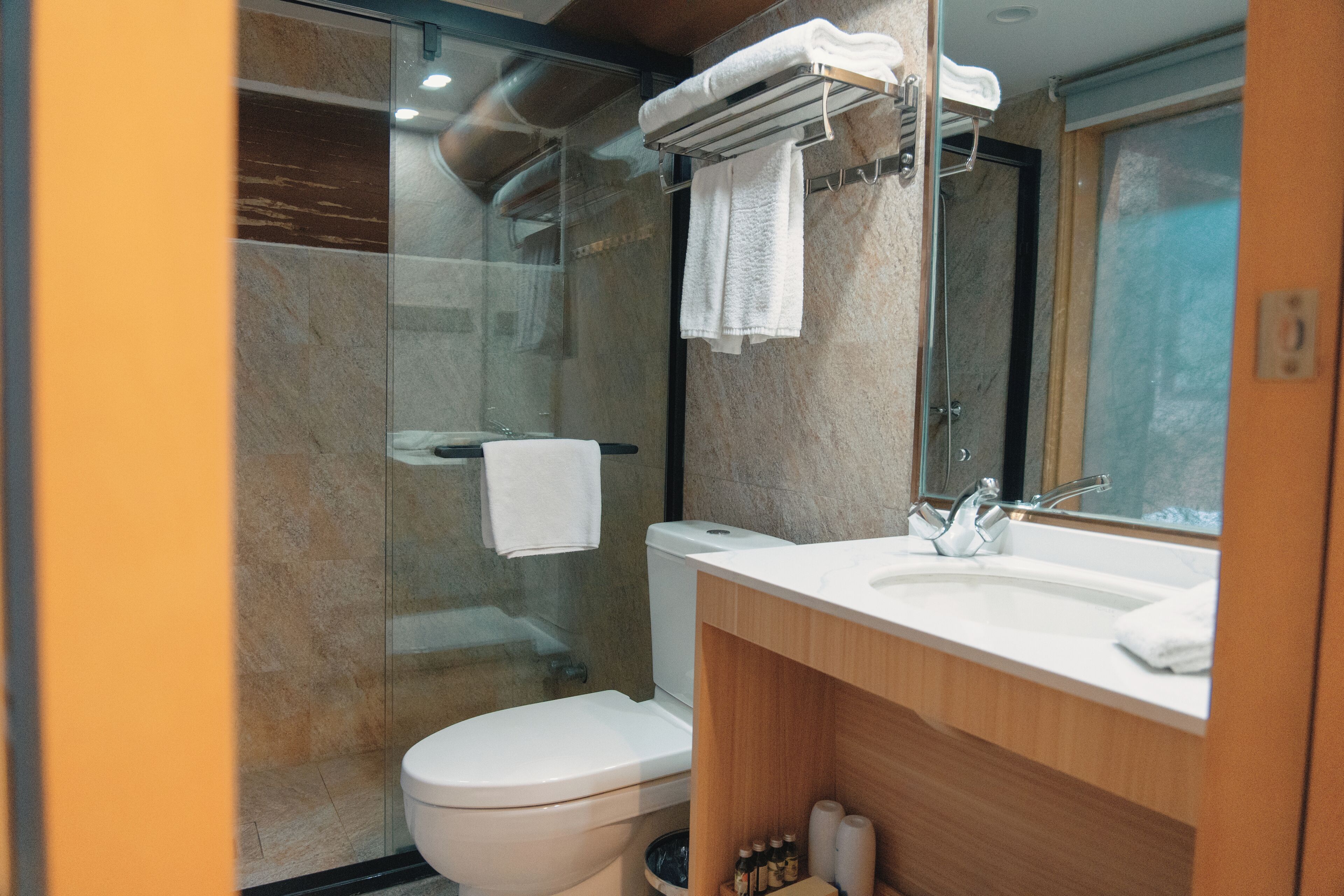 Une salle de bain moderne avec une douche à parois de verre, des toilettes blanches, un meuble-lavabo en bois et un miroir.