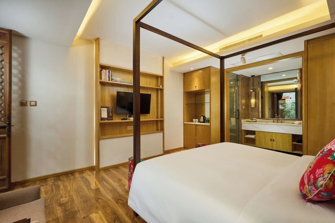A hotel room with a large bed, wooden shelving, a television, and a bathroom with a mirror and sink.