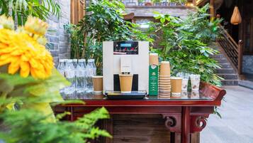 A coffee machine with disposable cups, a scale, and a green bottle on a wooden table with plants.