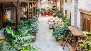 Un patio con plantas en macetas, mobiliario de madera y una estatua en el centro.
