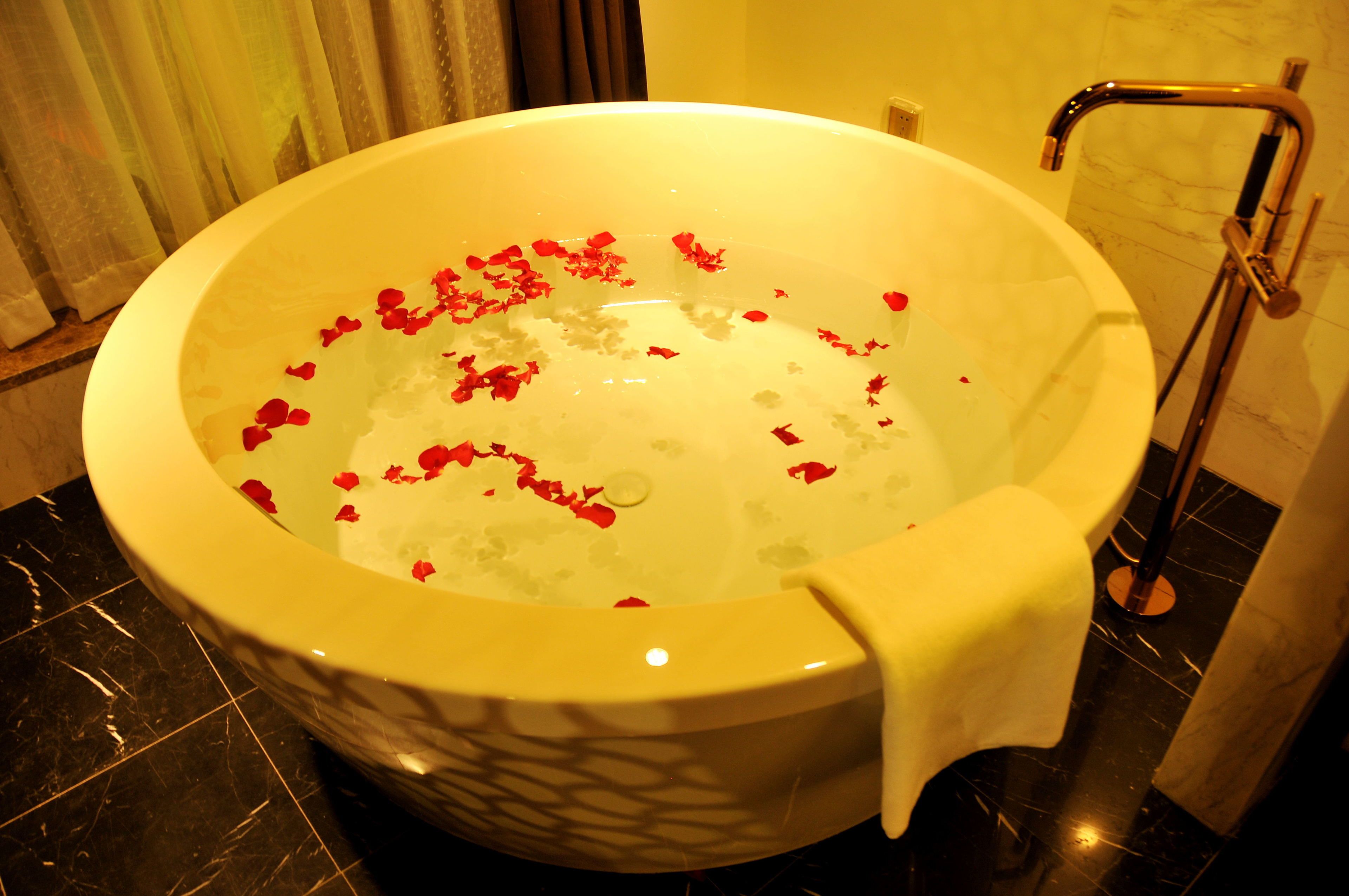 A large bathtub filled with water and rose petals, a showerhead, and a marble floor.