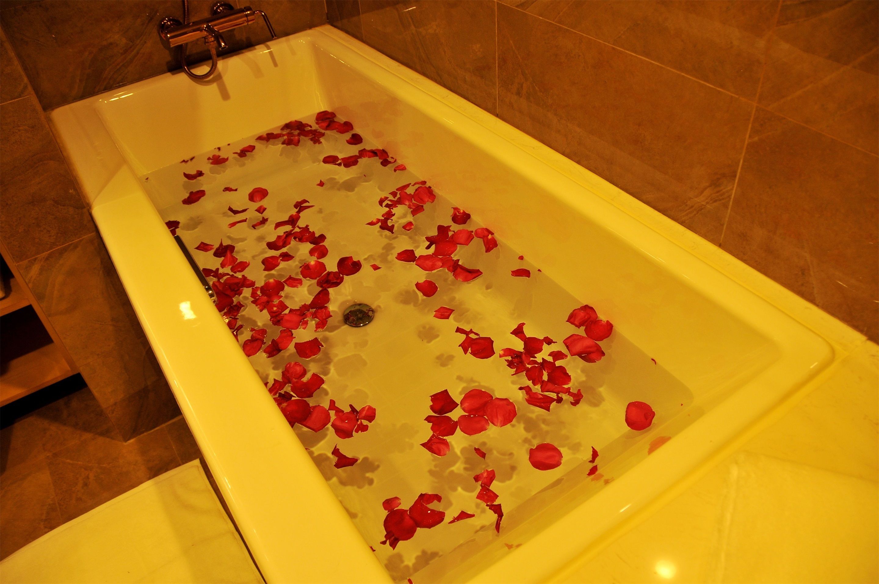 A bathtub filled with water and rose petals.