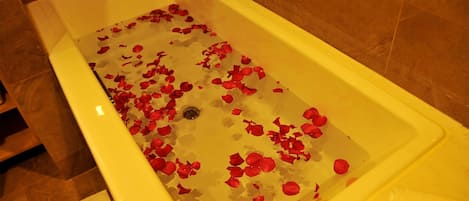 A bathtub filled with water and rose petals.