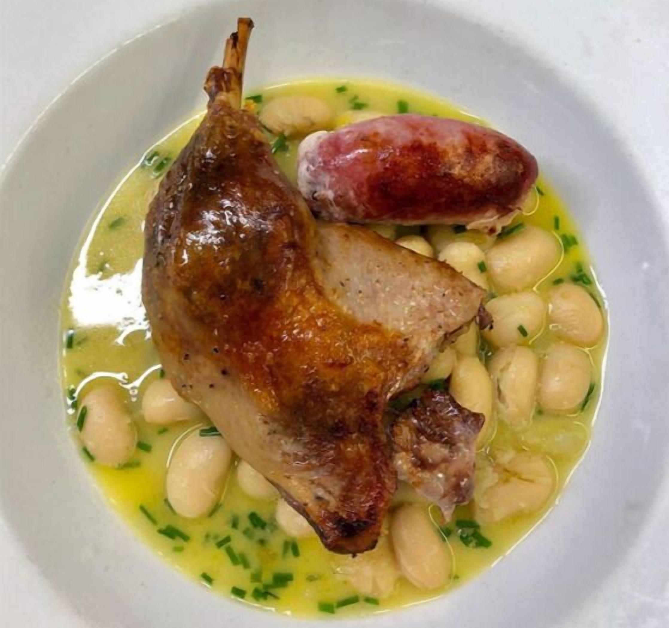 Ein Gericht mit gebratenem Fleisch, Wurst und Bohnen in einer weißen Schüssel.