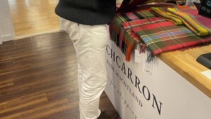 A person examining a colorful scarf at a store counter with a sign indicating the product is made in Scotland. - THE Gordon Arms Restaurant With Rooms (Selkirk)