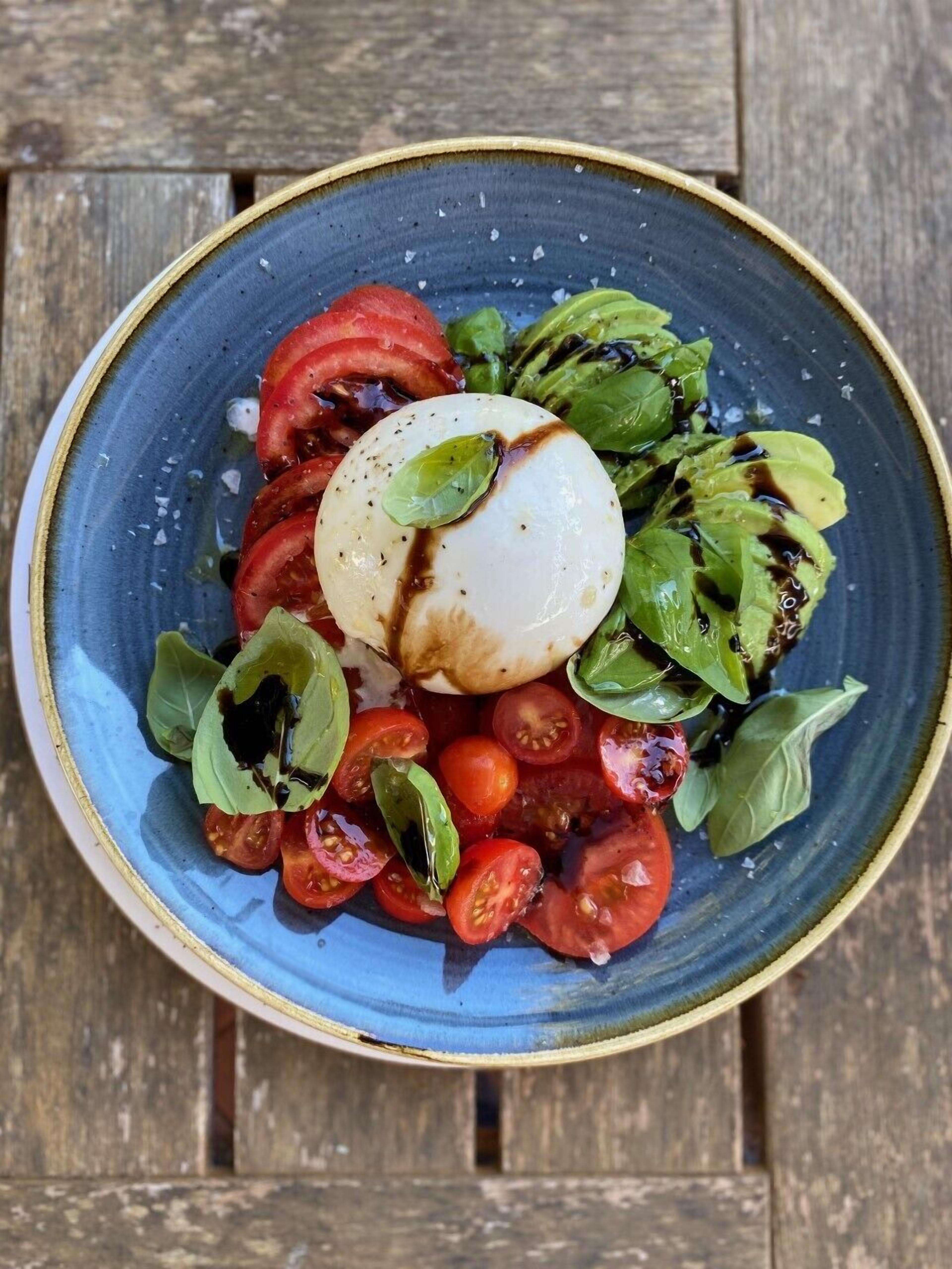 A bowl of Caprese salad with tomatoes, mozzarella, and basil on a blue plate.