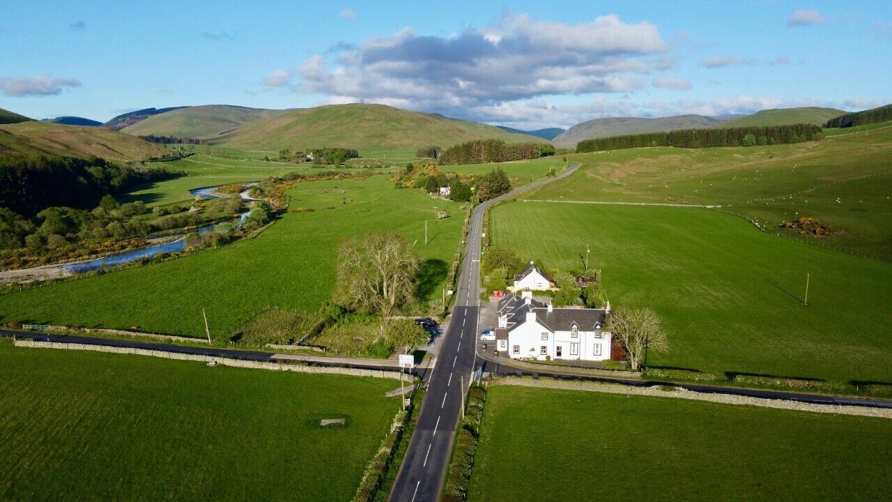 Paisaje rural con una casa blanca, una carretera y campos verdes.