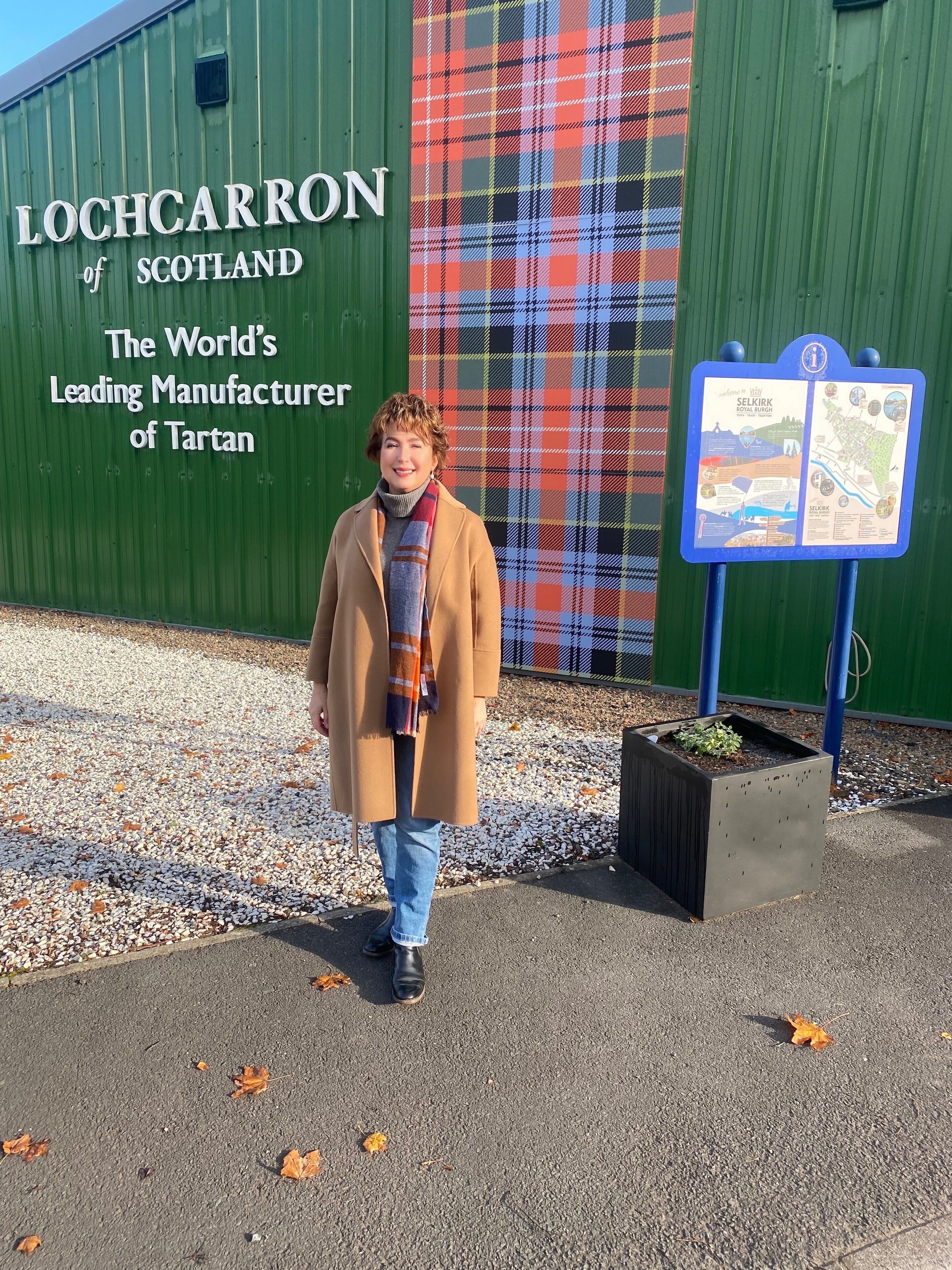 Una persona in piedi di fronte a un edificio con una parete a quadri e un cartello che recita “LOCHCARRON of SCOTLAND Produttore leader mondiale di tartan.”