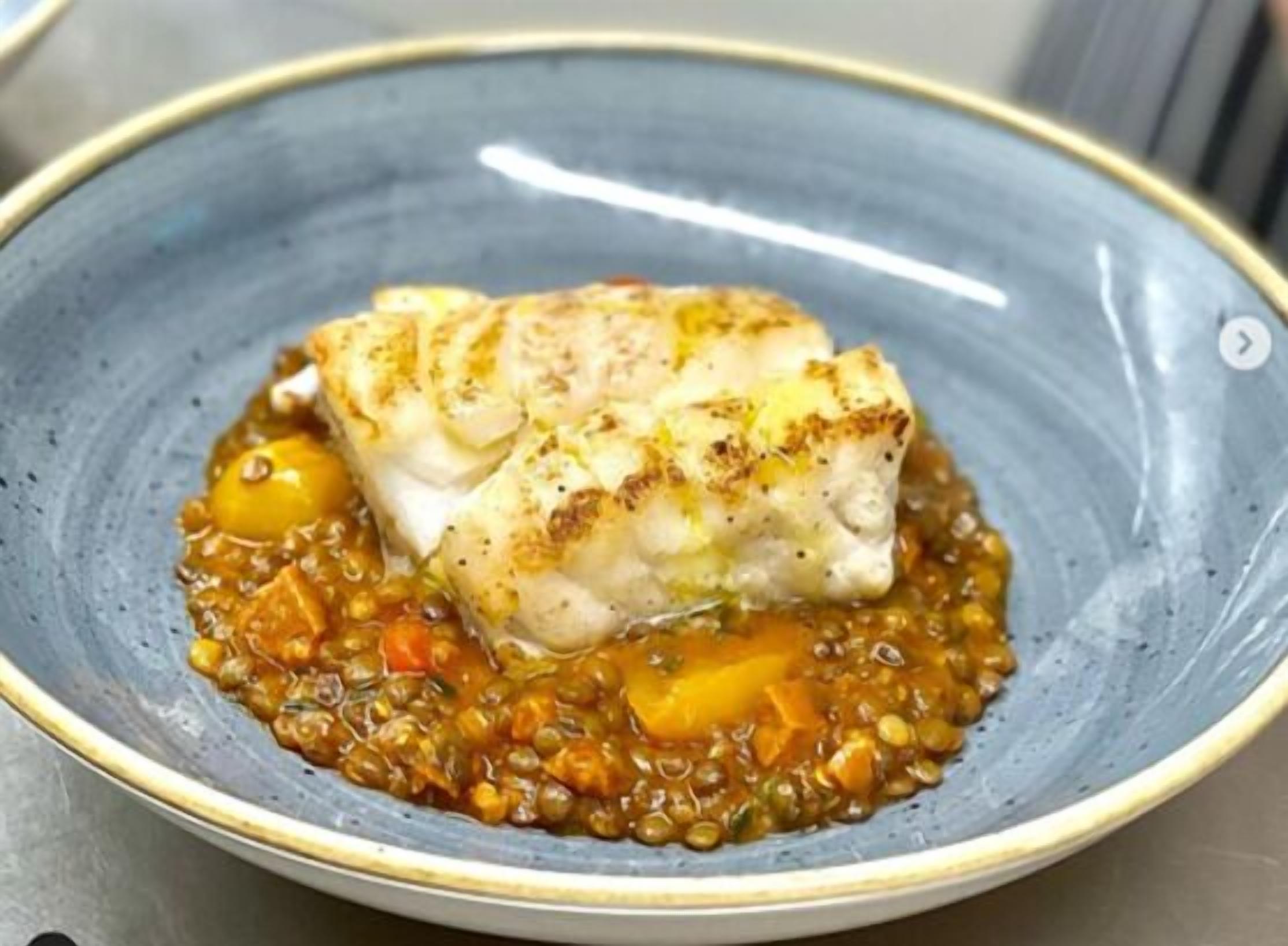 A plate with a piece of fish and lentil stew.