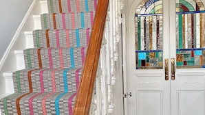 Un escalier orné d’une moquette colorée à motifs, de balustrades blanches et d’une main courante en bois.