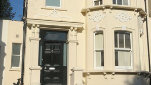 Un bâtiment  à deux étages avec une porte d’entrée noire, des moulures blanches et un escalier menant à l’entrée.
