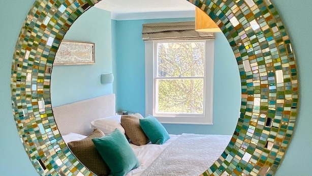 Une chambre à coucher avec un lit, des oreillers, une fenêtre et un miroir fixé au mur.