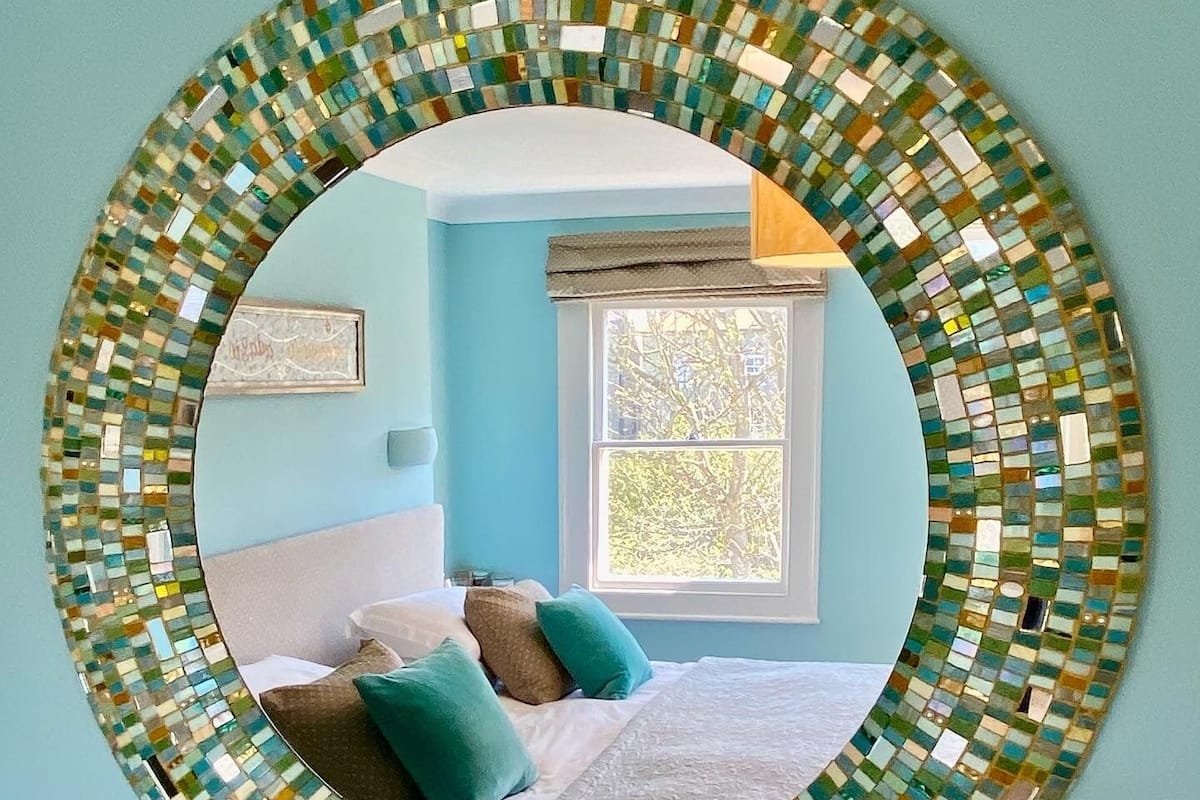 A bedroom with a bed, pillows, a window, and a wall-mounted mirror.