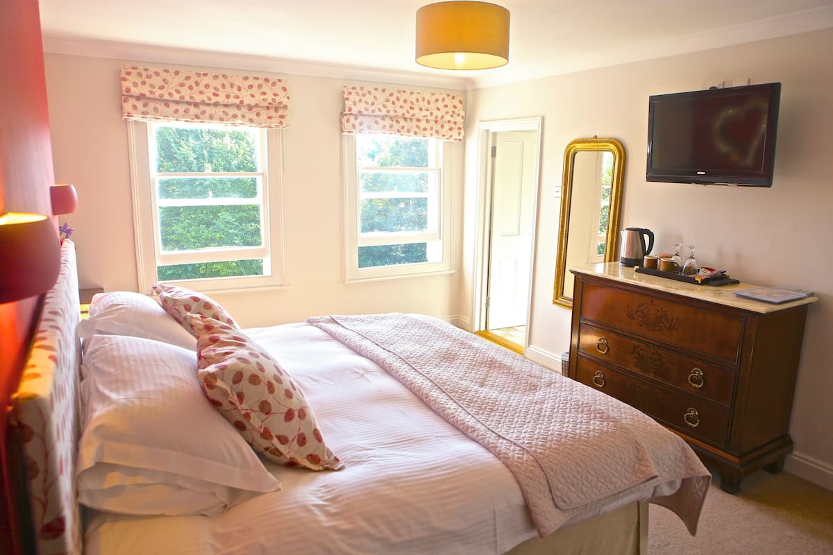 A bedroom with a bed, dresser, mirror, and a television on the wall.