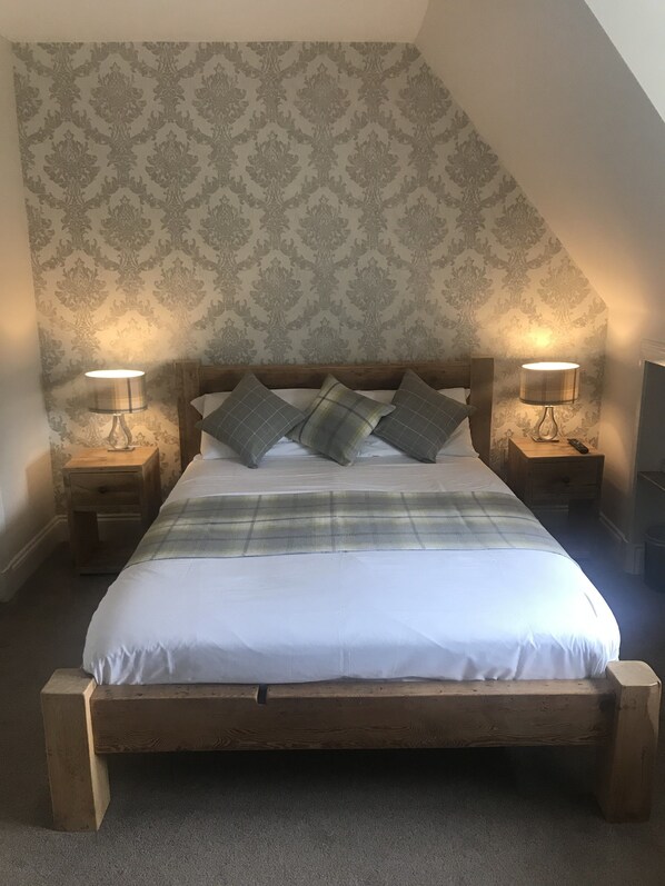 A bedroom with a large bed, two bedside tables with lamps, a wooden headboard, and patterned wallpaper.