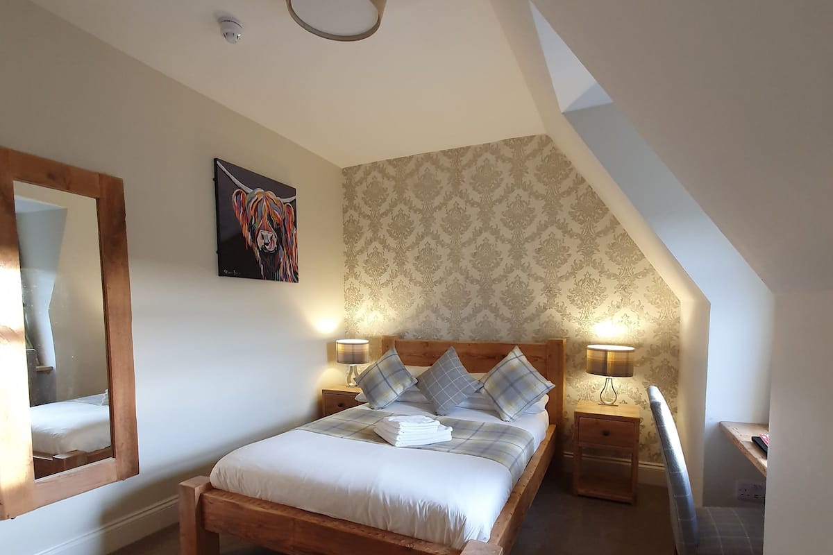 A bedroom with a wooden bed, a mirror, a desk, and a lamp.