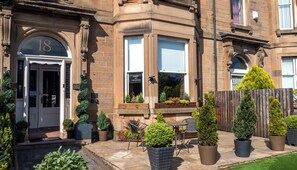 A traditional building with a number 18 sign, a 'Sorry No Vacancies' sign, and a well-maintained garden with potted plants and outdoor seating.