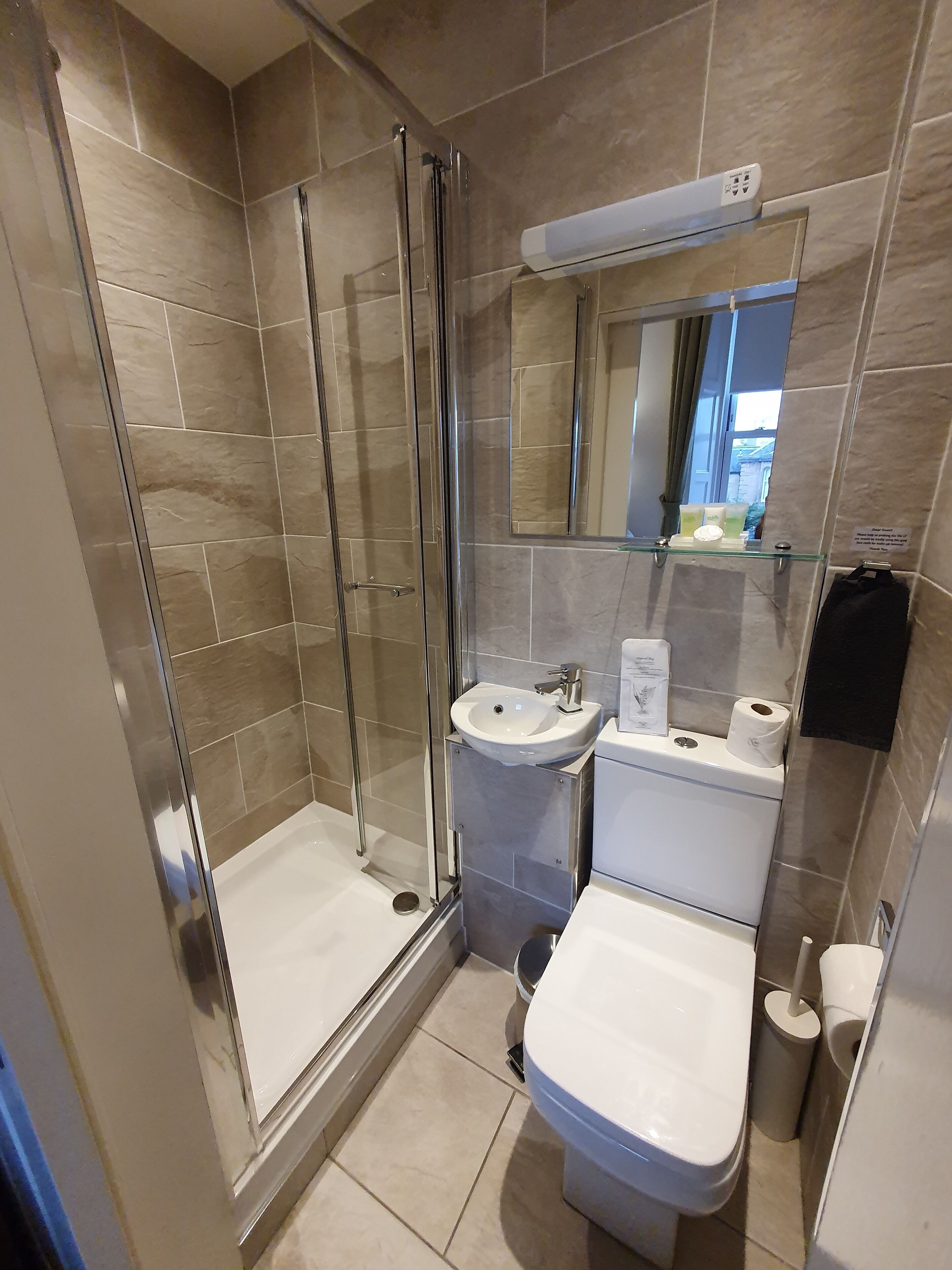 Moderni kylpyhuone, jossa on lasiseinällä varustettu suihku, jalkapallin muotoinen pesuallas ja wc.
