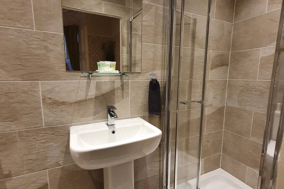 A bathroom with a pedestal sink, a mirror, and a glass-enclosed shower.