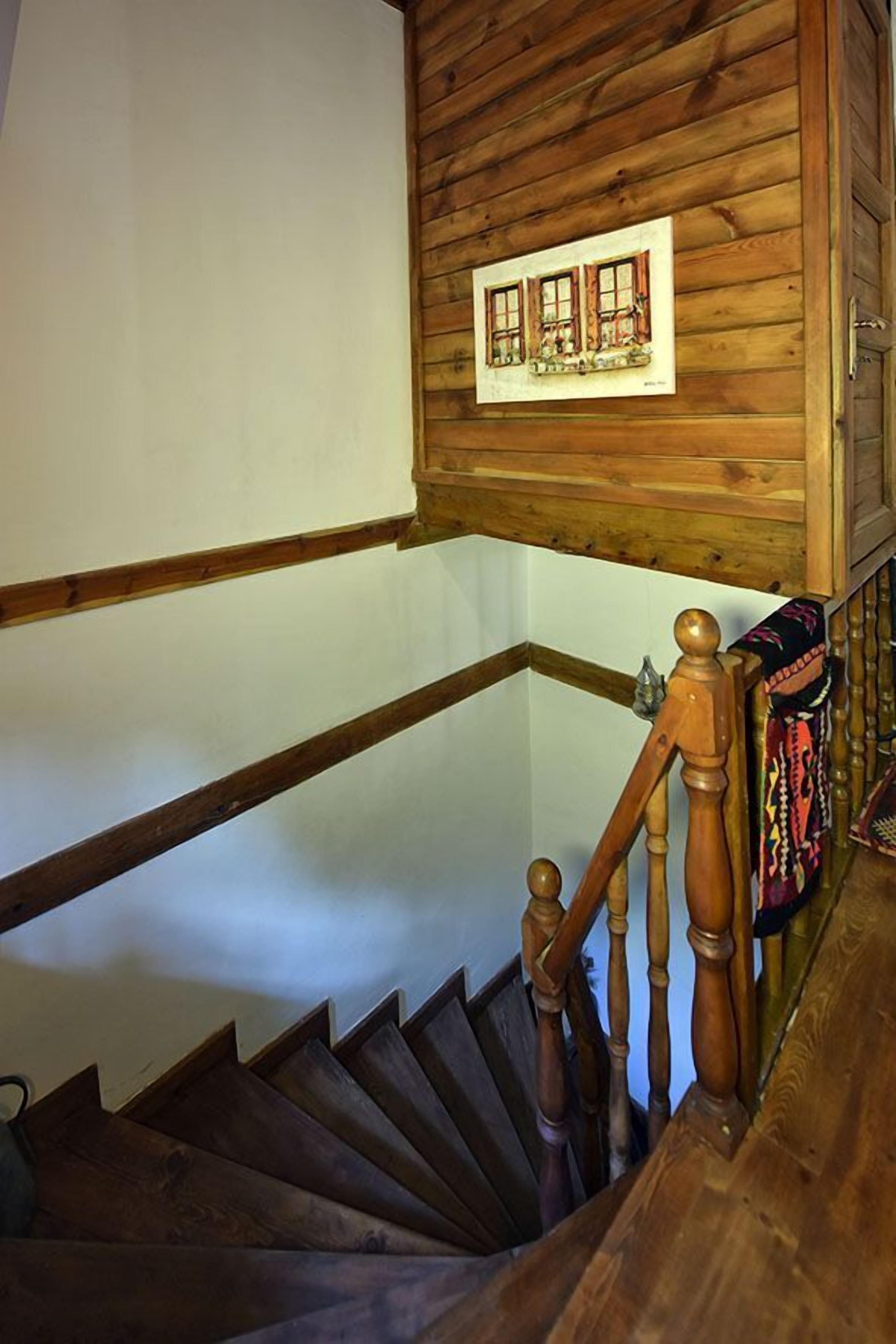 Una escalera de madera con barandilla y un cuadro de una casa en la pared superior.