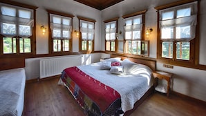 A spacious bedroom with a large bed, wooden beams on the ceiling, and multiple windows with curtains. - Dadibra Konak (Safranbolu)