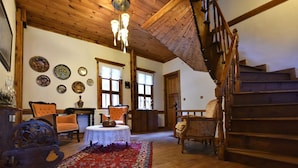A spacious room with wooden flooring, a red patterned rug, and a staircase with wooden railings. - Dadibra Konak (Safranbolu)