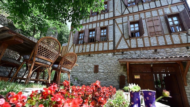A traditional half-timbered building with a stone facade, a wooden door, and a garden with red flowers and a wicker chair. - Dadibra Konak (Safranbolu)