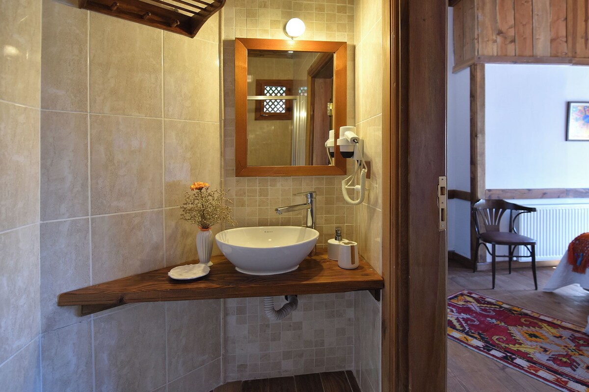 A bathroom with a large white sink, a wooden countertop, a mirror, and a vase with flowers.