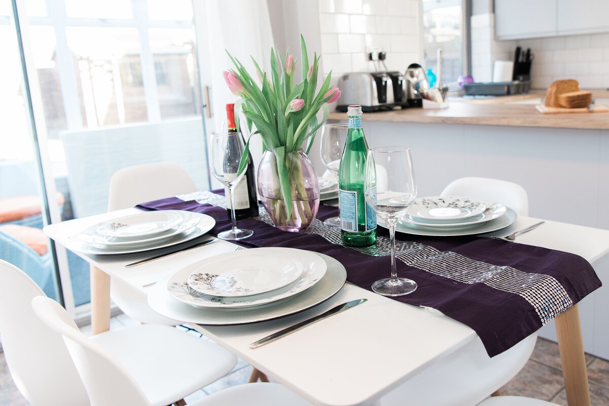 A dining table set with plates, glasses, and a vase of flowers.