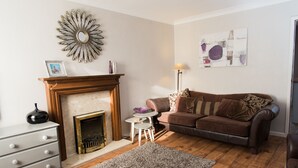 A living room with a fireplace, a brown leather sofa, a small round table, and a decorative wall piece. - Abbey House (Towcester)