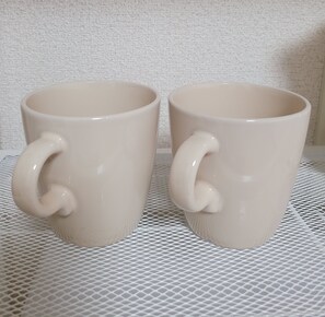 Zwei beige Keramiktassen mit Henkeln auf einer weißen, strukturierten Oberfläche.