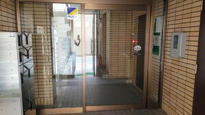 Corredor com porta de vidro que dá para um quarto, paredes revestidas de azulejos e teto com iluminação embutida.