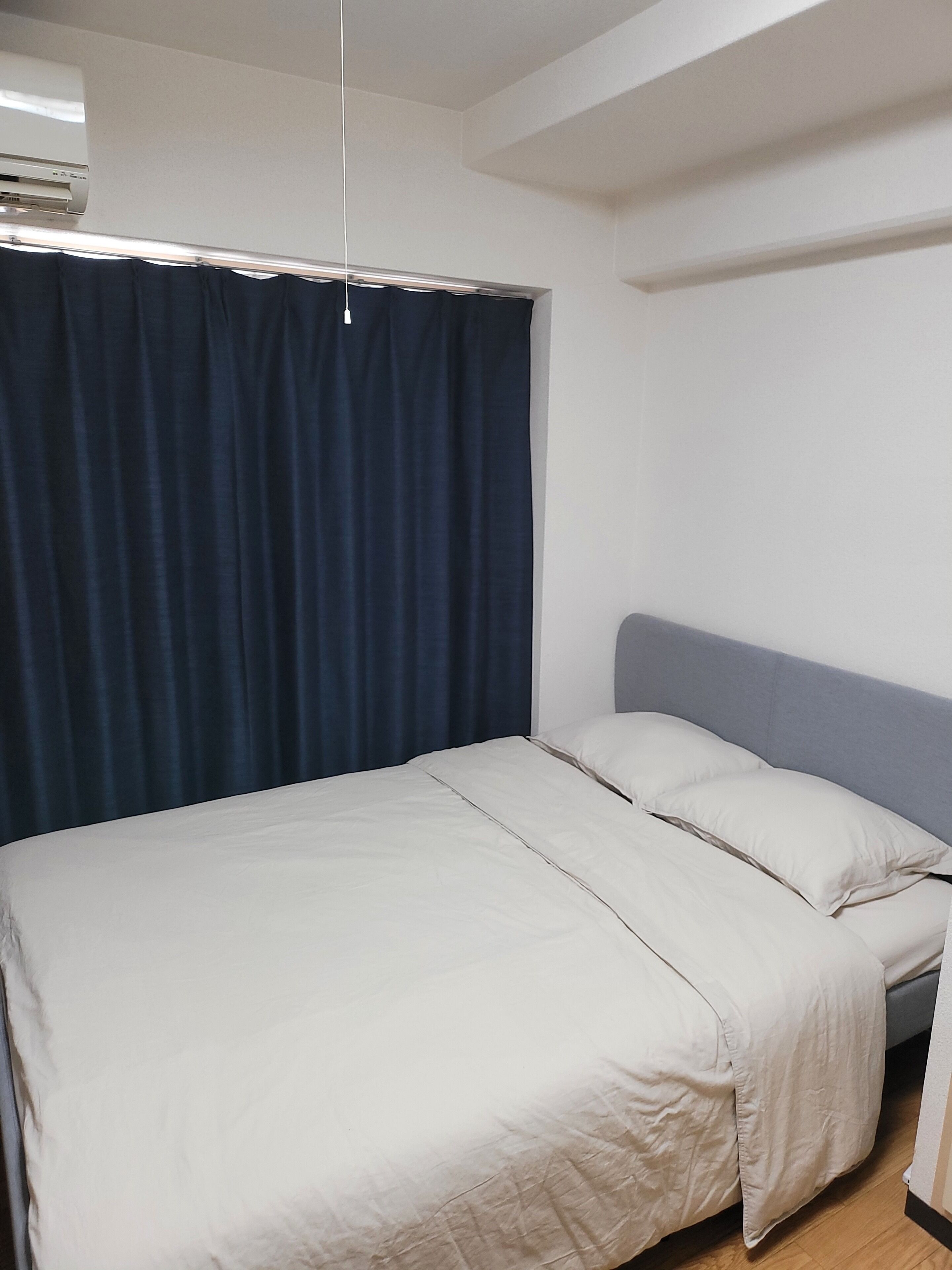 A room with a bed, a headboard, a curtain, and a ceiling-mounted air conditioning unit.