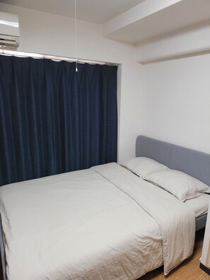 Ein Zimmer mit einem Bett, einem Kopfteil, einem Vorhang und einer Decken-Klimaanlage.