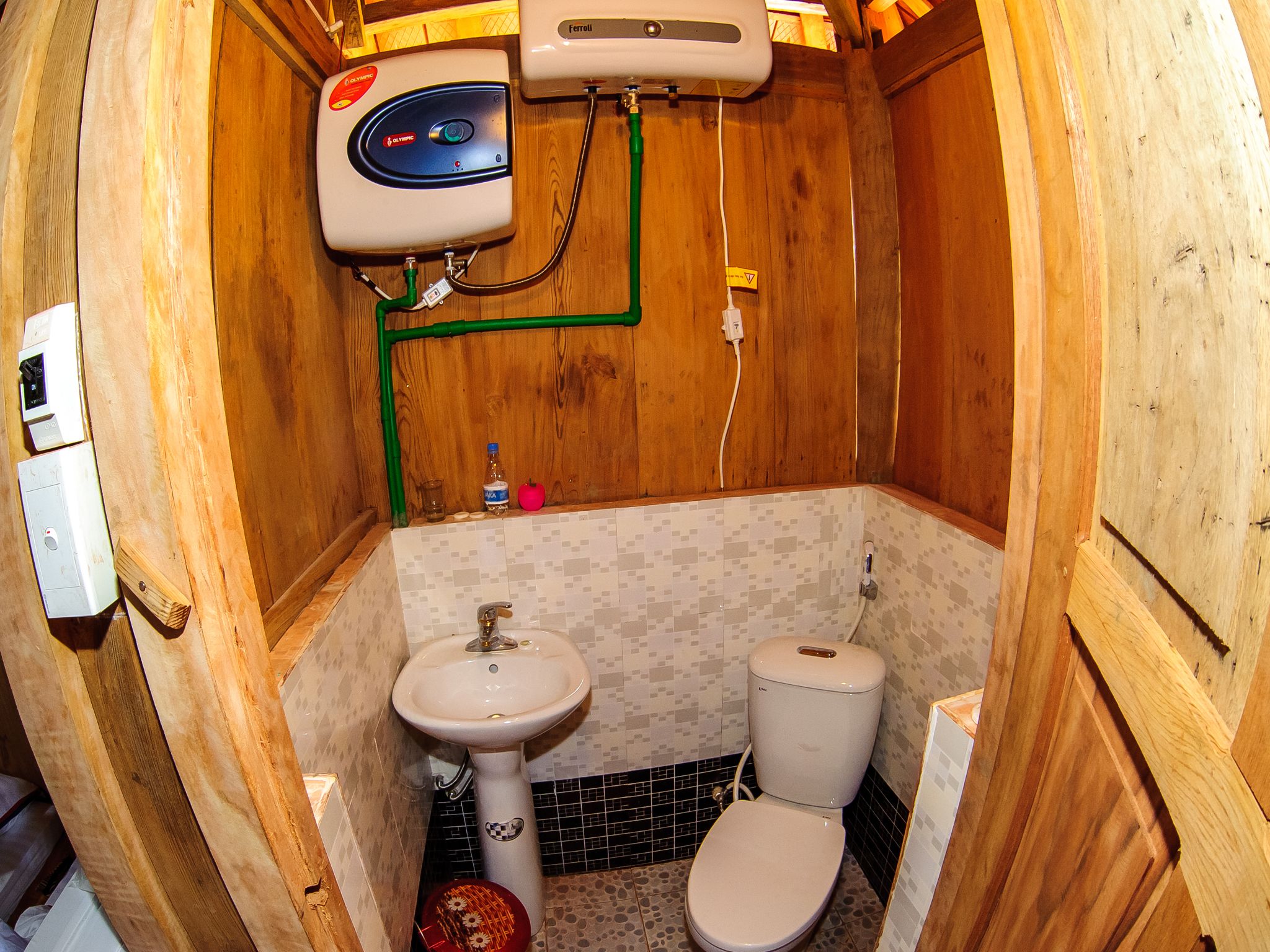 A small, wooden bathroom with a toilet, sink, and a water heater.