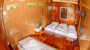 Quarto de cabana de madeira com duas camas, uma mesinha com uma planta e paredes de madeira.