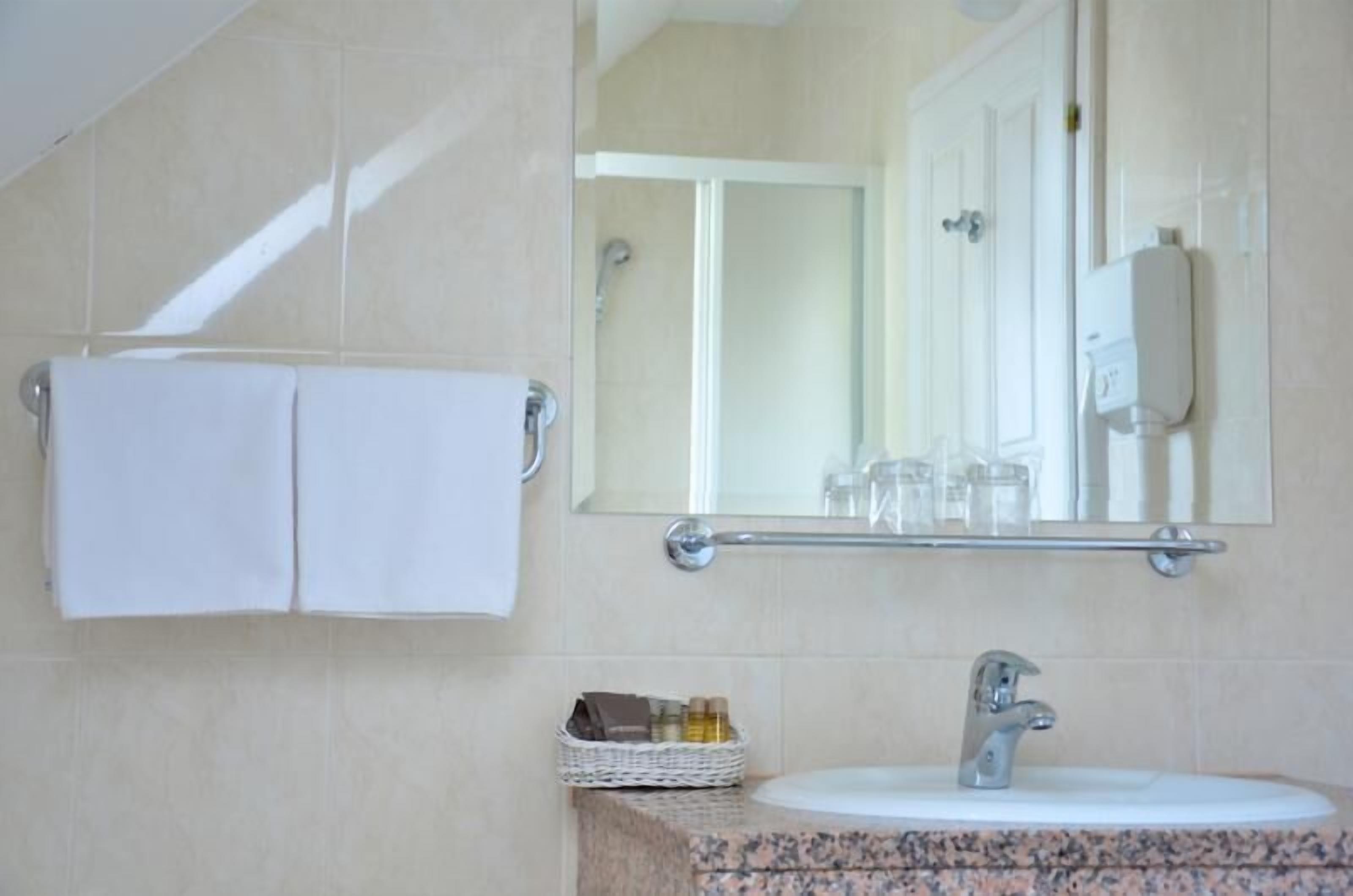Een badkamer met een wastafel, spiegel, handdoekrek en een mandje met toiletartikelen.