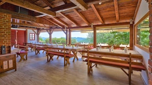 A rustic dining area with wooden tables and benches, brick walls, and large windows offering a view of greenery. - Vuglec Breg (Krapina)