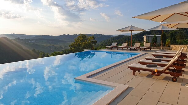 An infinity pool with lounge chairs and umbrellas, overlooking a mountainous landscape. - Vuglec Breg (Krapina)