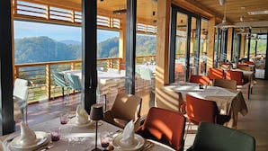 A restaurant with large windows offering mountain views, wooden interior, and multiple dining tables. - Vuglec Breg (Krapina)