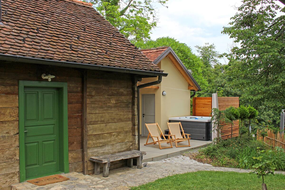 A rustic building with a green door, a wooden bench, and two lounge chairs outside.