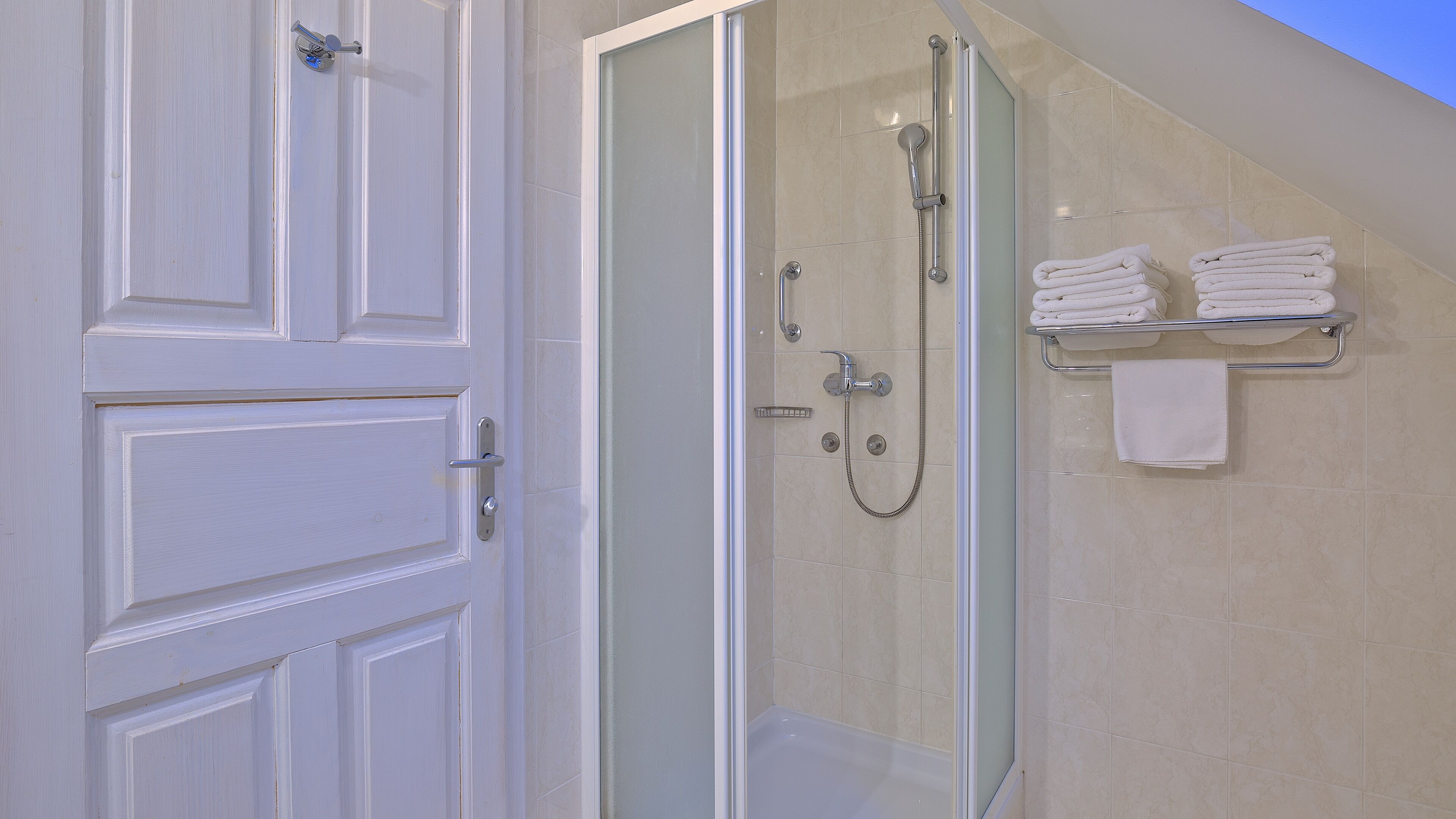 A bathroom with a glass-enclosed shower, a towel rack with folded towels, and a white door.