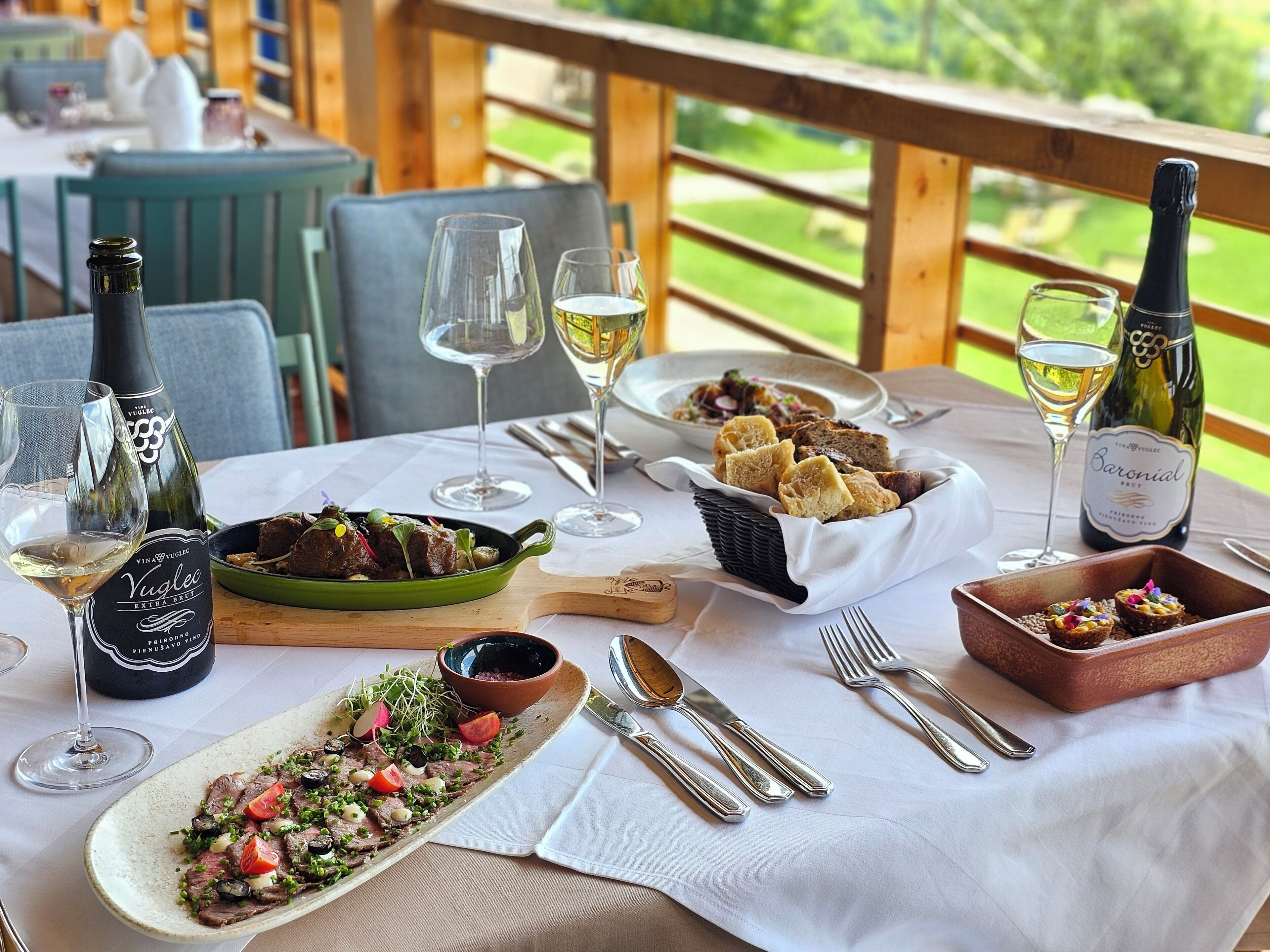 Una mesa de comedor dispuesta con varios platos, copas de vino y botellas.